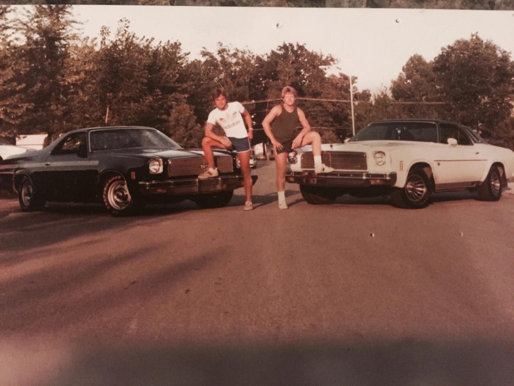 Younger Dodd and friend in front of cars