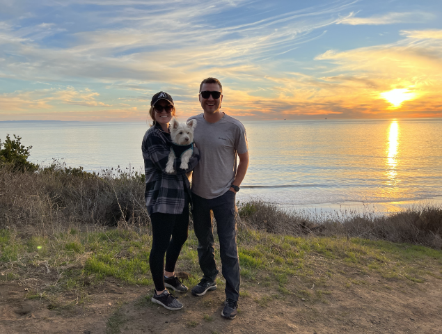 man woman and dog in front of shoreline